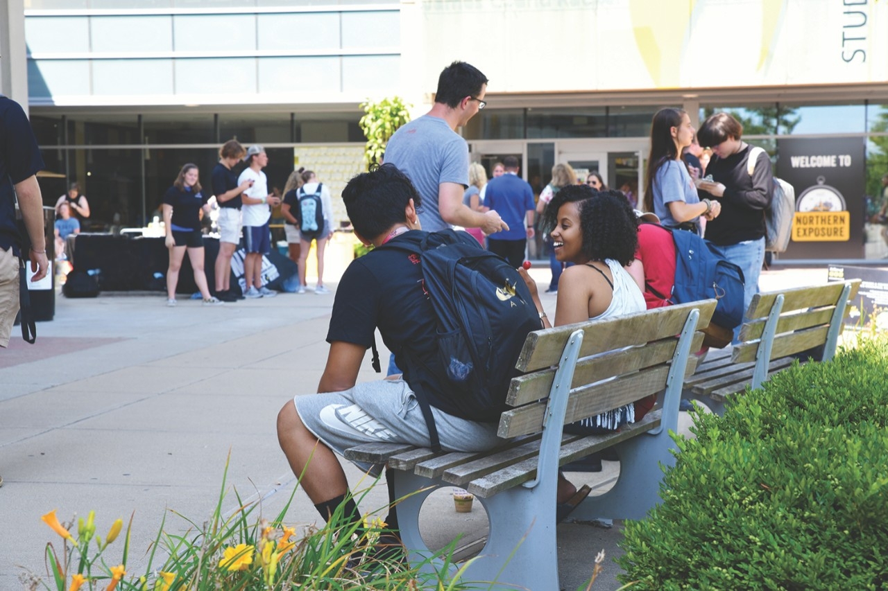 Students sitting on bench outside of the Student Union, talking to each other.